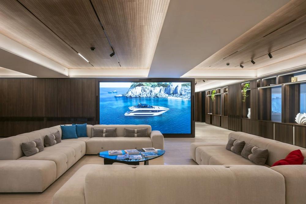 Salone di uno yacht con divani, tavolo e grande schermo integrato nella parete.